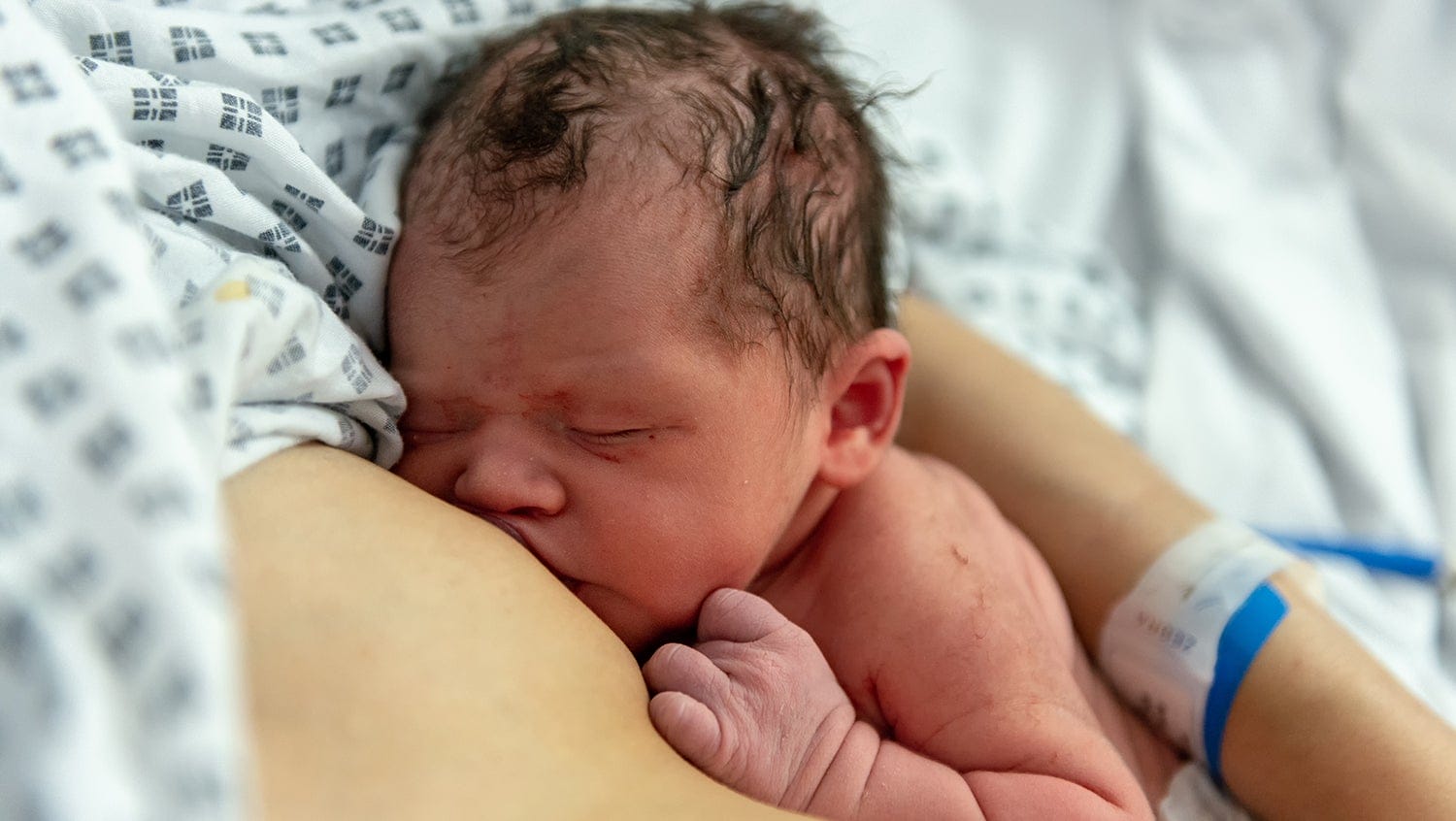 A newborn baby is breastfeeding during rooming-in with mom at the hospital