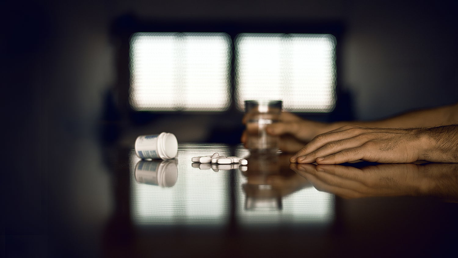 Man's hands seen on table with pill bottle of buprenorphine as part of ongoing treatment after detox.