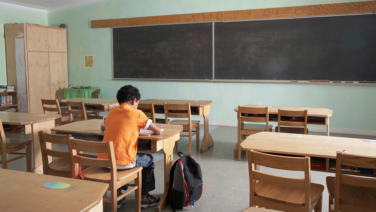 View from back of classroom of young boy sitting at a desk in the empty classroom