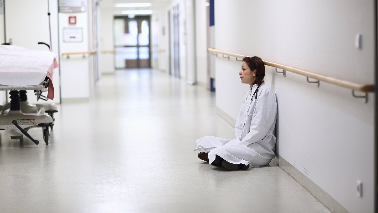Doctor in white lab coat sits distressed on the floor of the hospital hallway