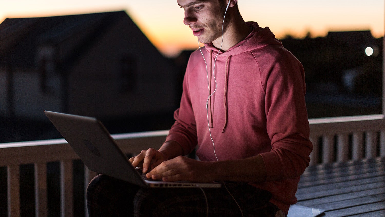 Young man sits outside with laptop and headphones to gain privacy for telehealth appointment