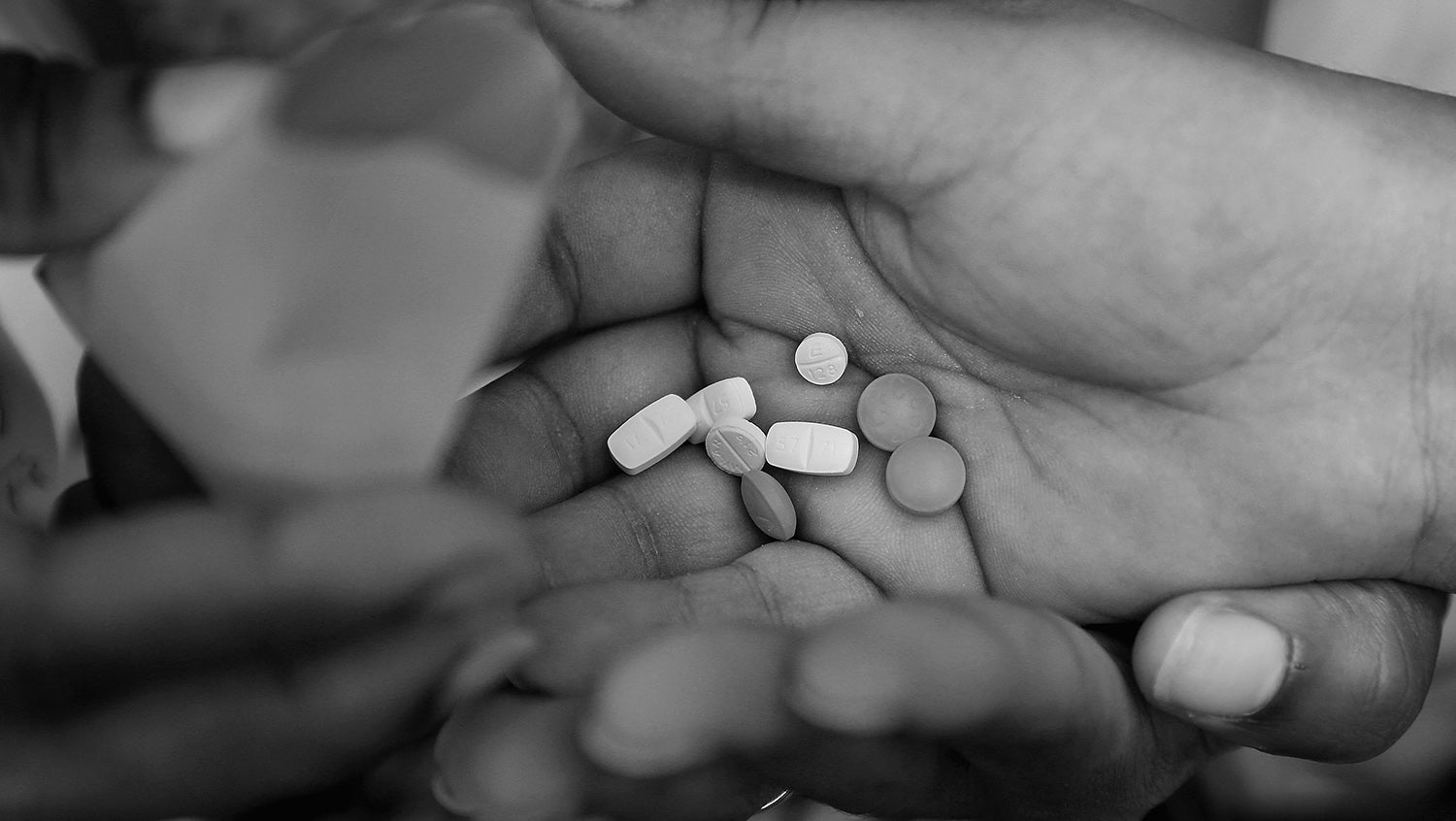 Black and white photo of patient's hand receiving medications for HIV