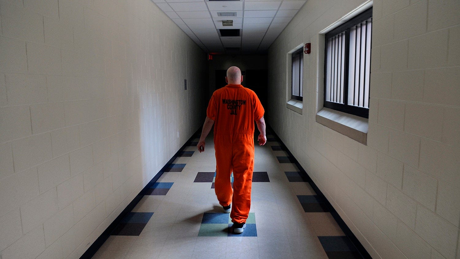 Man in orange jumpsuit walks down prison hallway