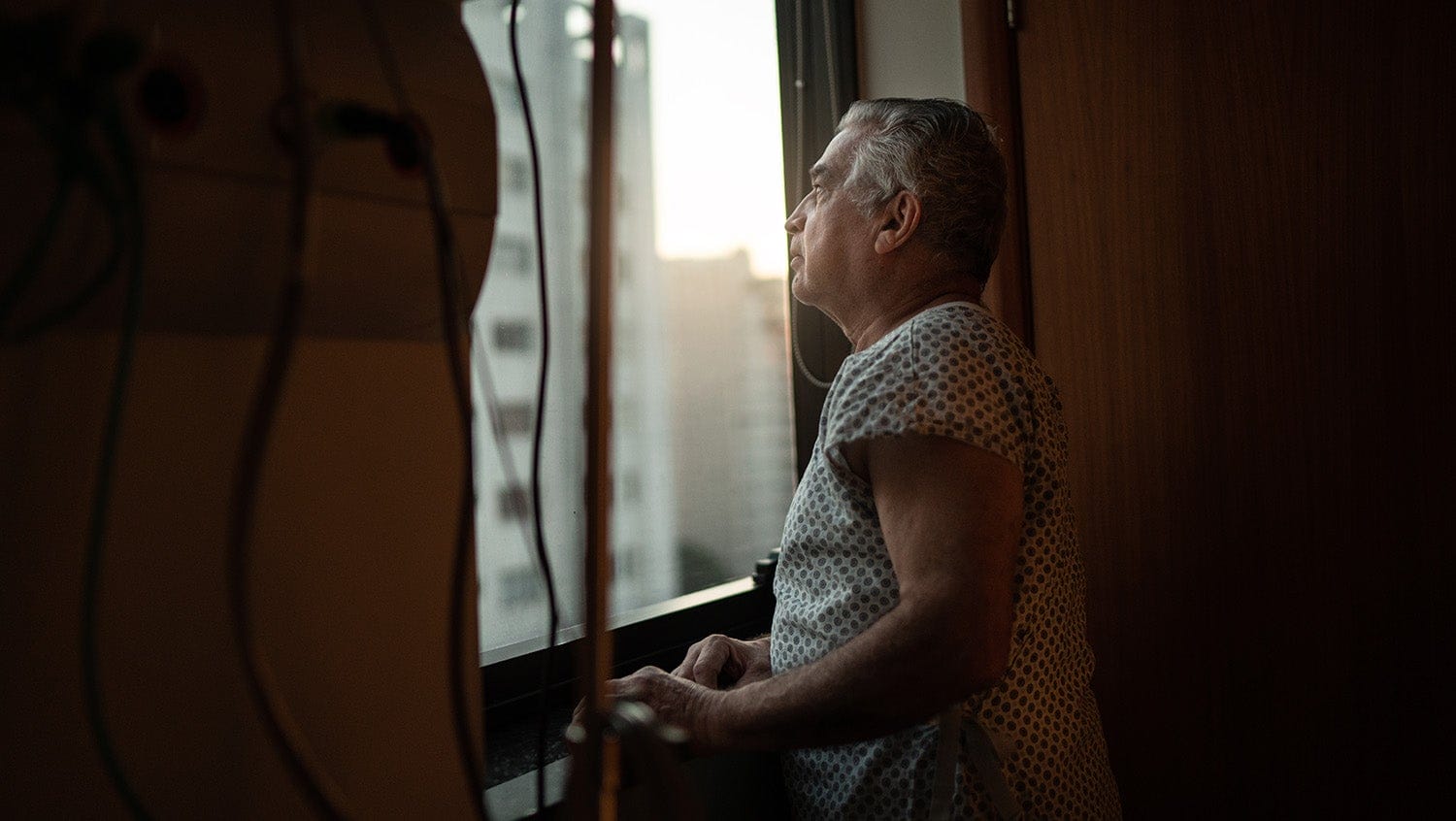 Man in hospital gown looks out room window