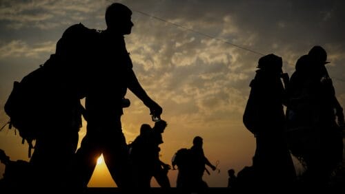 A group of refugees walk through the desert at dusk