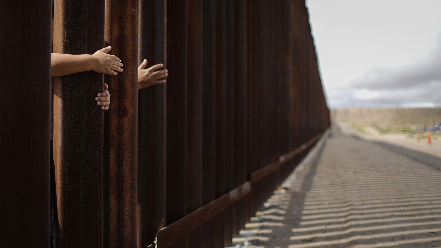 Hands reach through the wall at the US Mexico border