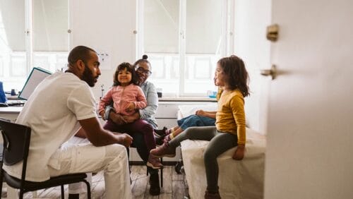 Smiling mother and daughter looking at male pediatrician consulting girls at medical clinic