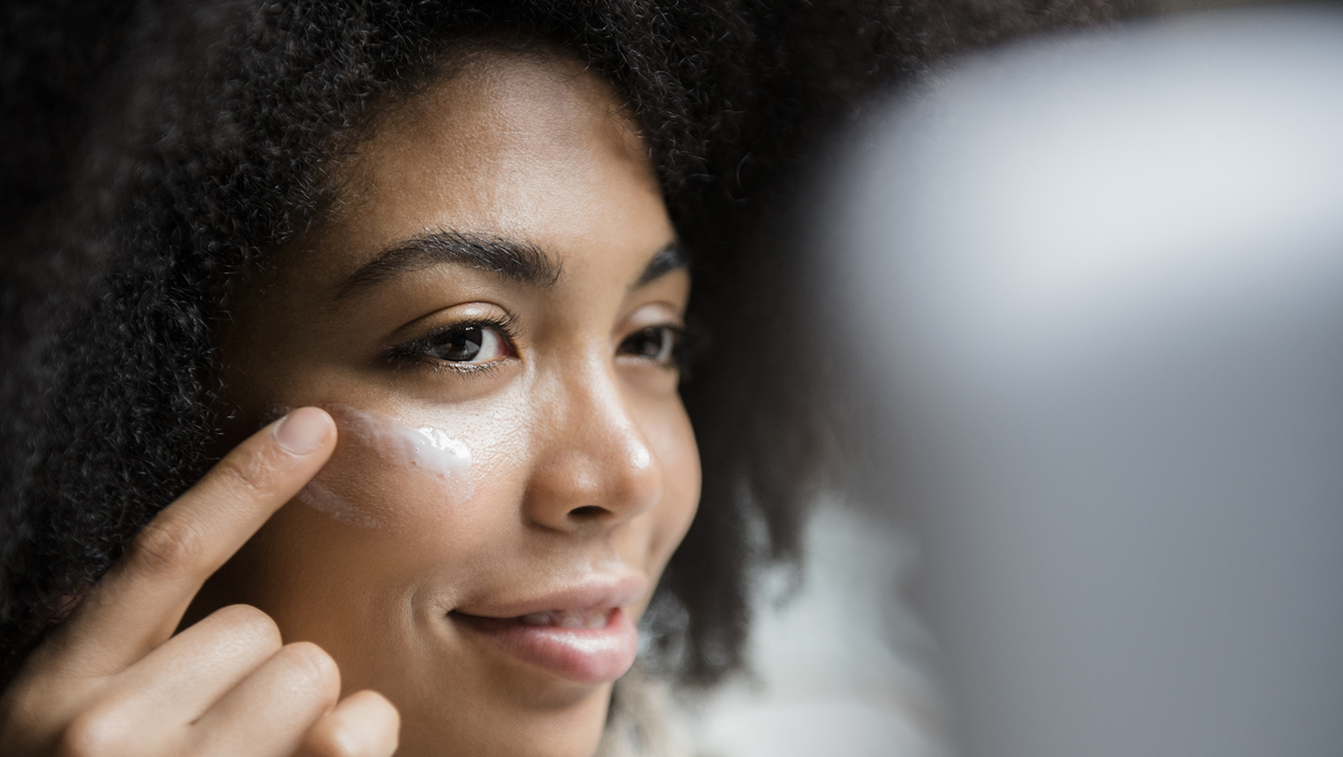 Woman of color putting on tinted sunscreen for dark skin under her eyes