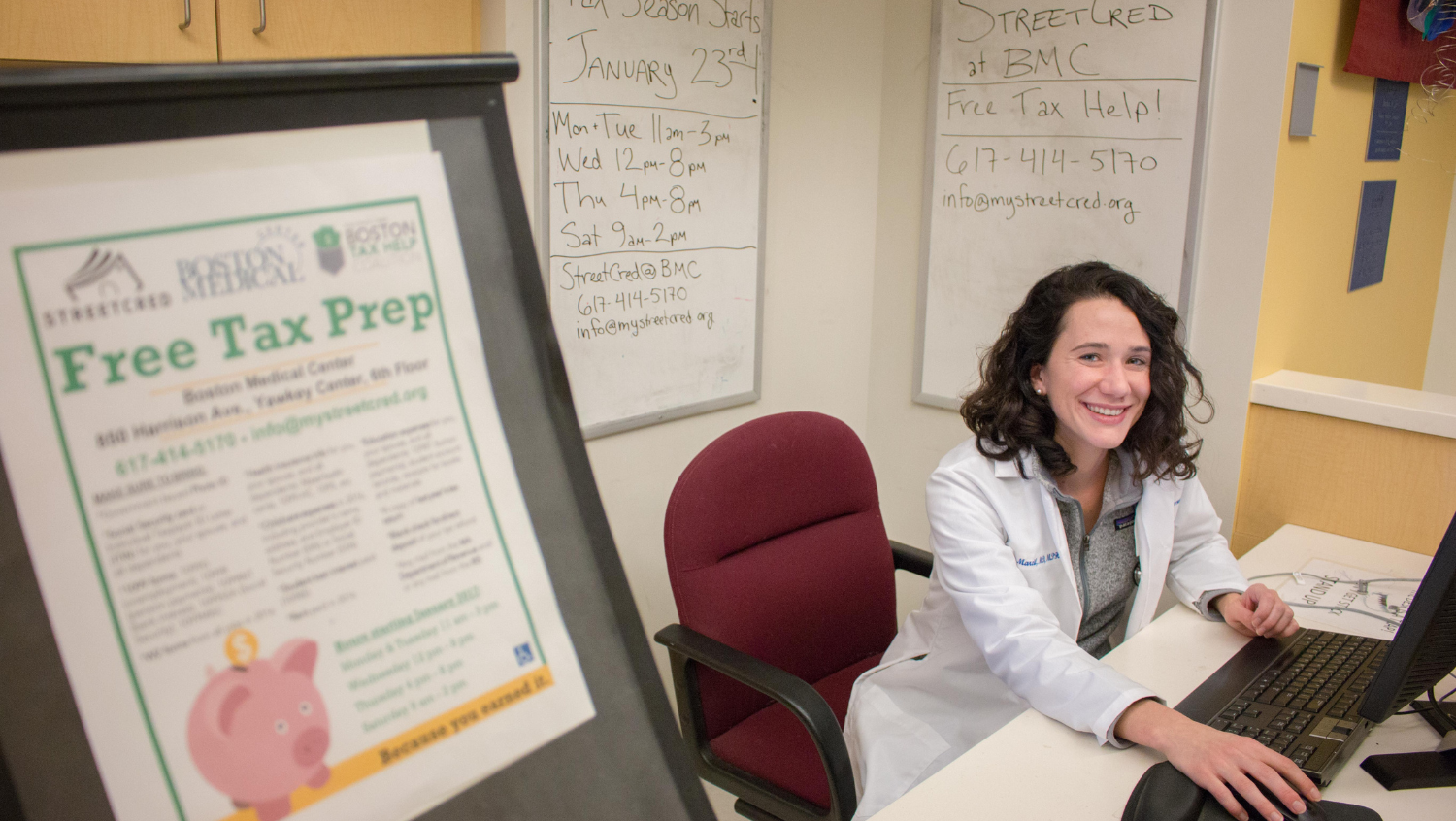 Photo of Lucy Marcil with 'Free Tax Prep' poster about antipoverty medicine