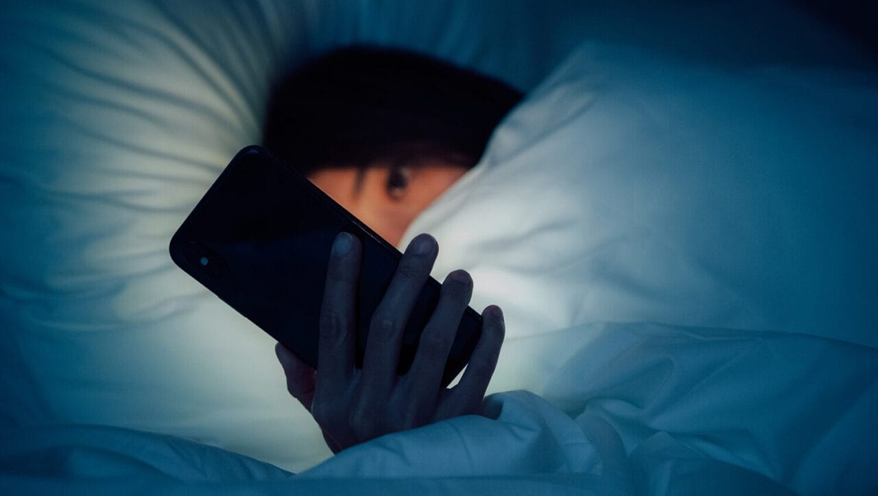 a close up of a woman in bed in the dark scrolling through tiktok on her phone