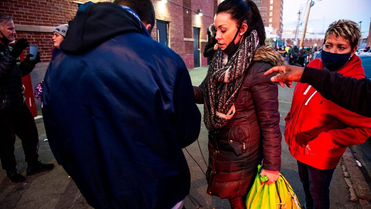 on the street, a post overdose outreach program worker hands supplies to a man