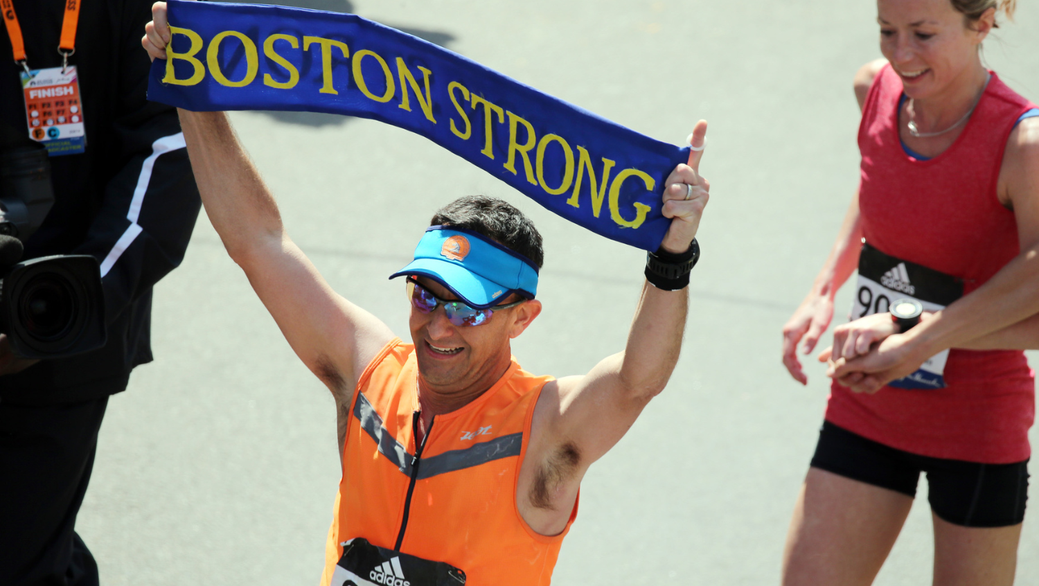 a man is running in an orange outfit, carrying a sign "boston strong"