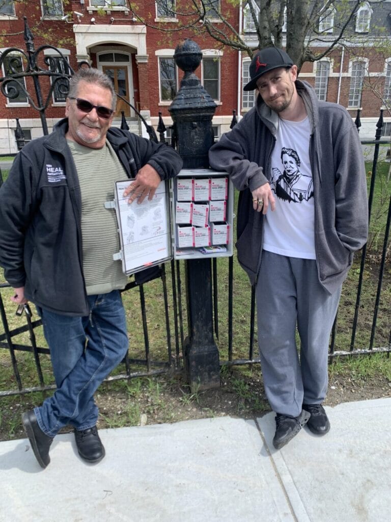 two men pose in front of a lock box containing naloxone, also known as Narcan, an opioid overdose reversal medication