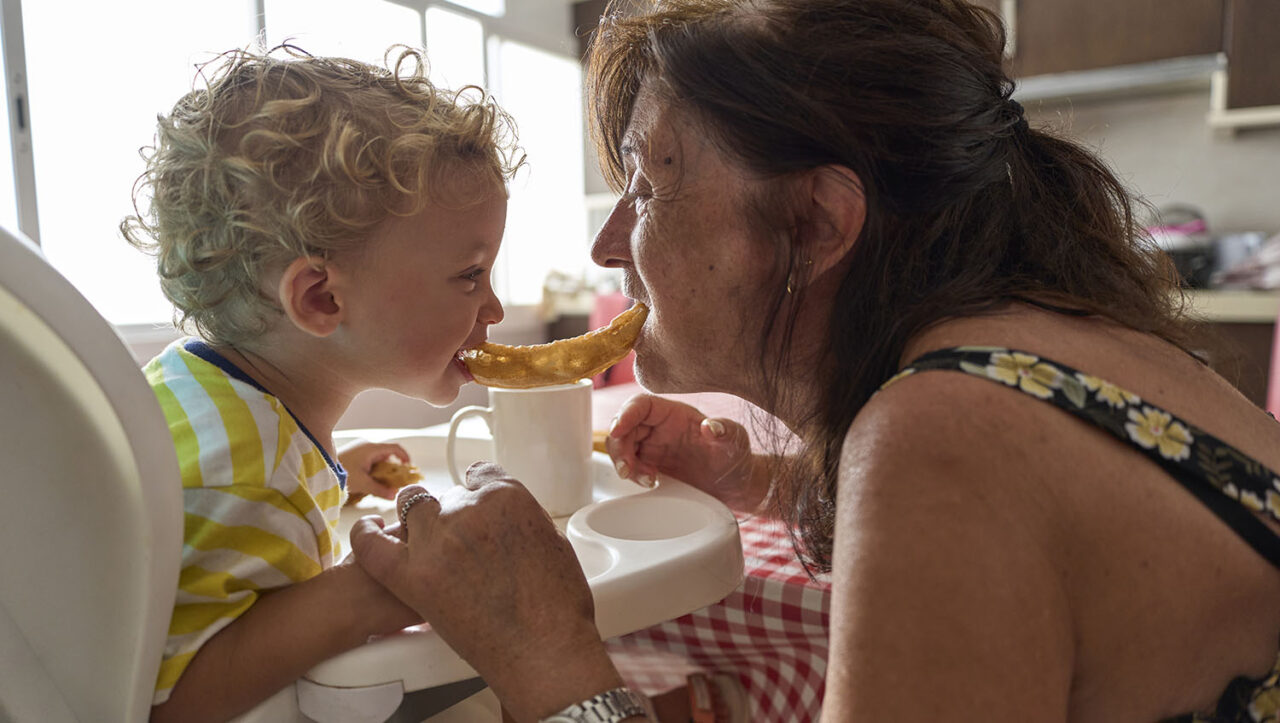 Senior woman grandmother sharing churros with her 20 month old grandson at home.