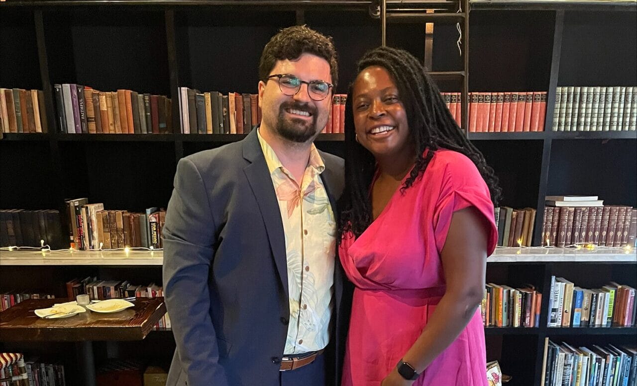 AJ Mell and Monica Germain standing next to each other in front of a bookcase at the health equity fellowship graduation