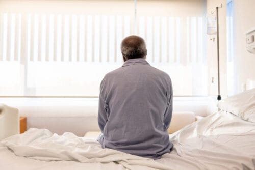 Sick man sitting on the bed at the hospital and feeling depressed - healthcare and medicine concepts