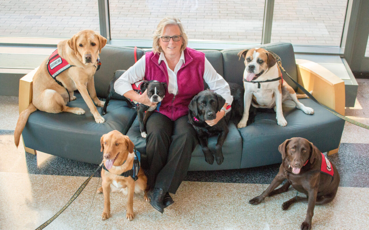 woman sitting on the couch at the center surrounded by therapy dogs