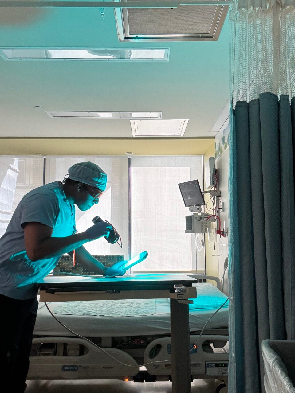 image of a man in scrubs in a hospital room examining a tray table with a light