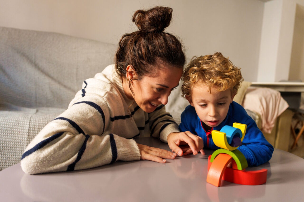Mother and son playing with a wooden stacking toy on a table. Learning and development through creative play at home