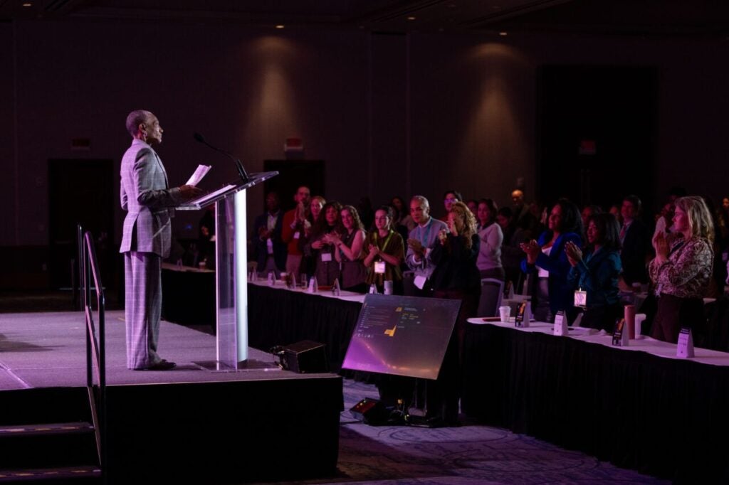 dr. thea james speaks at a podium at EQTY 2026 with a view over an audience